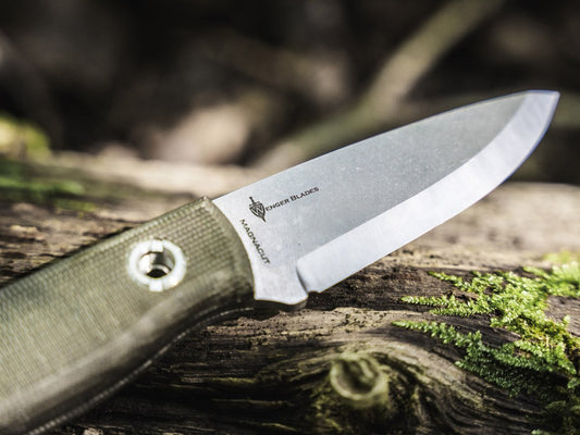 Scandi ground bushcraft knife with green canvas Micarta handle resting on a mossy log in the forest