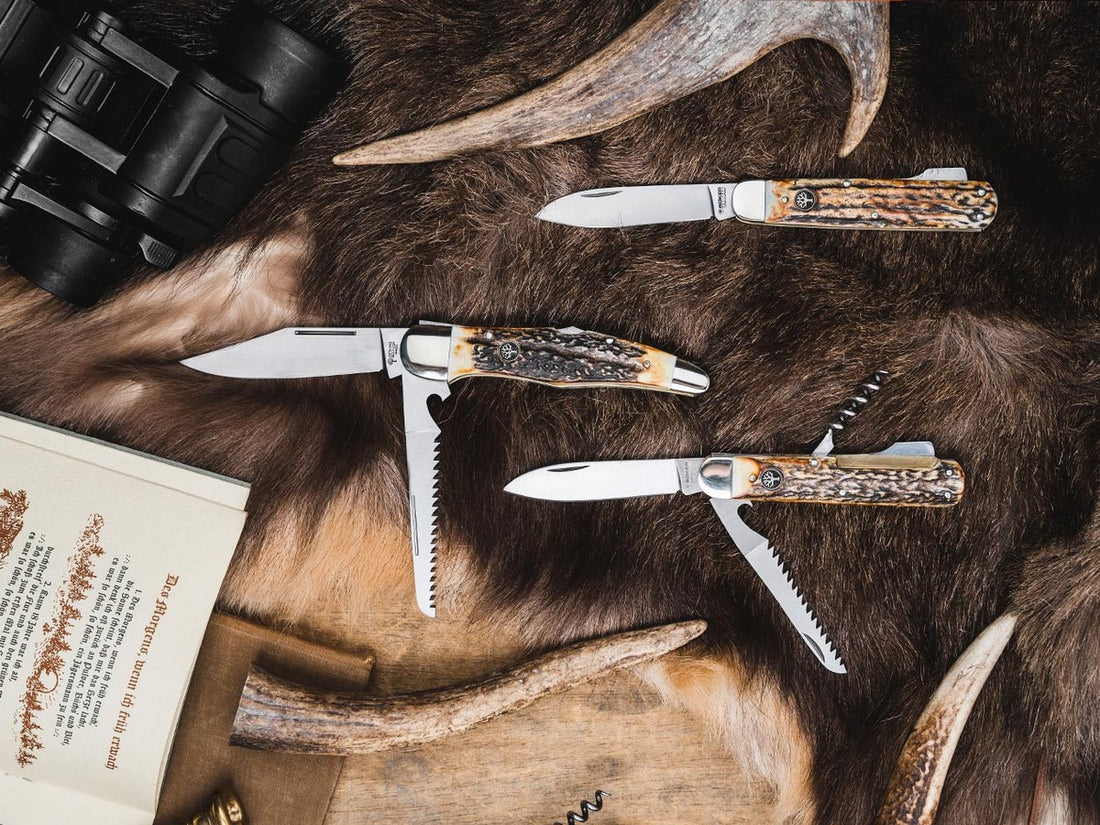 Traditional hunting pocket knives with stag handles, saw blades and corkscrew on a fur with antlers and binoculars