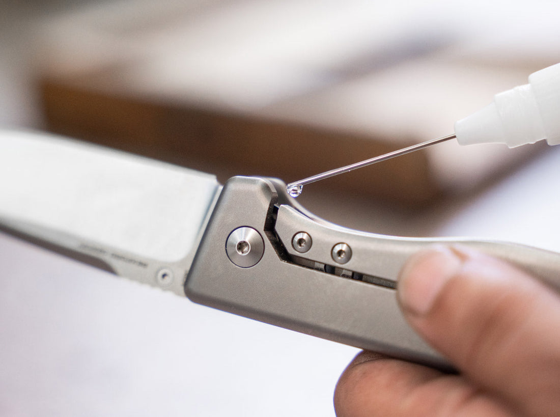 A drop of knife oil from a precision applicator being placed on the pivot of an open titanium folding knife