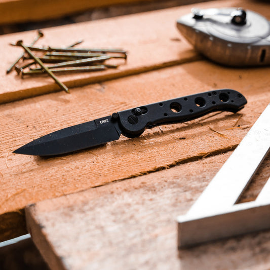 CRKT folding knife with black blade on a workbench next to nails and a tape measure